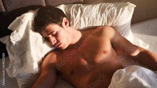 Handsome shirtless young man in bed sleeping and waking up