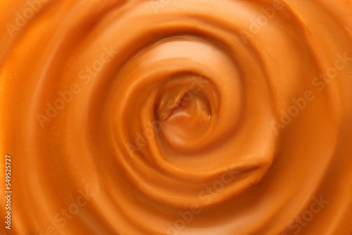 Liquid melted caramel syrup. Background of caramel syrup, paste. Curl, wave of caramel. Texture, Close up, top view.