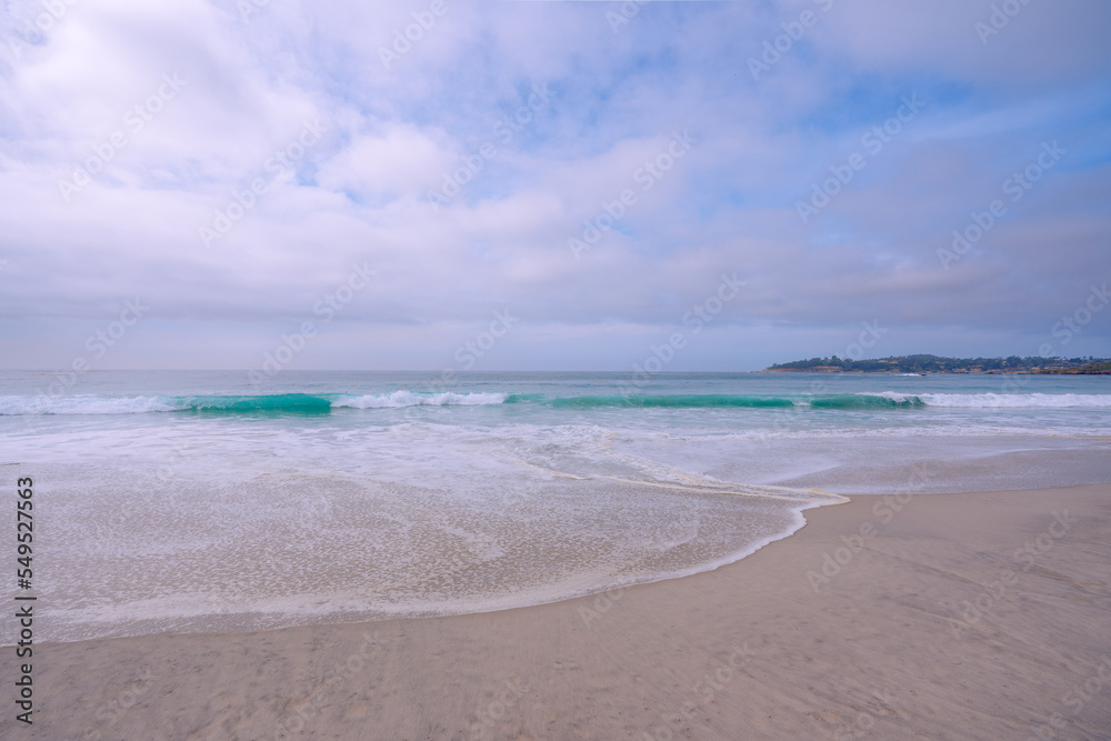 Light airly seascape in blue and pink colors. Wide sandy beach, sea waves, and cloudy sky