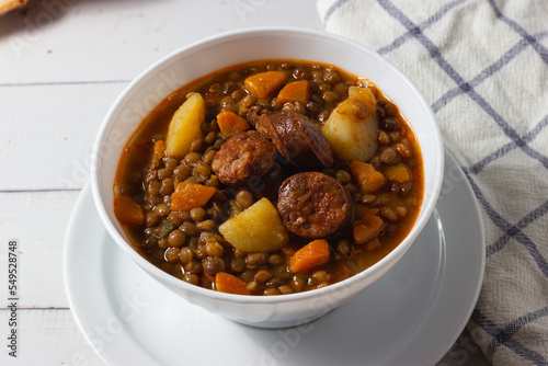 Traditional lentil soup with legs, carrots and chorizo on a white on a white background. Mediterranean cuisine.