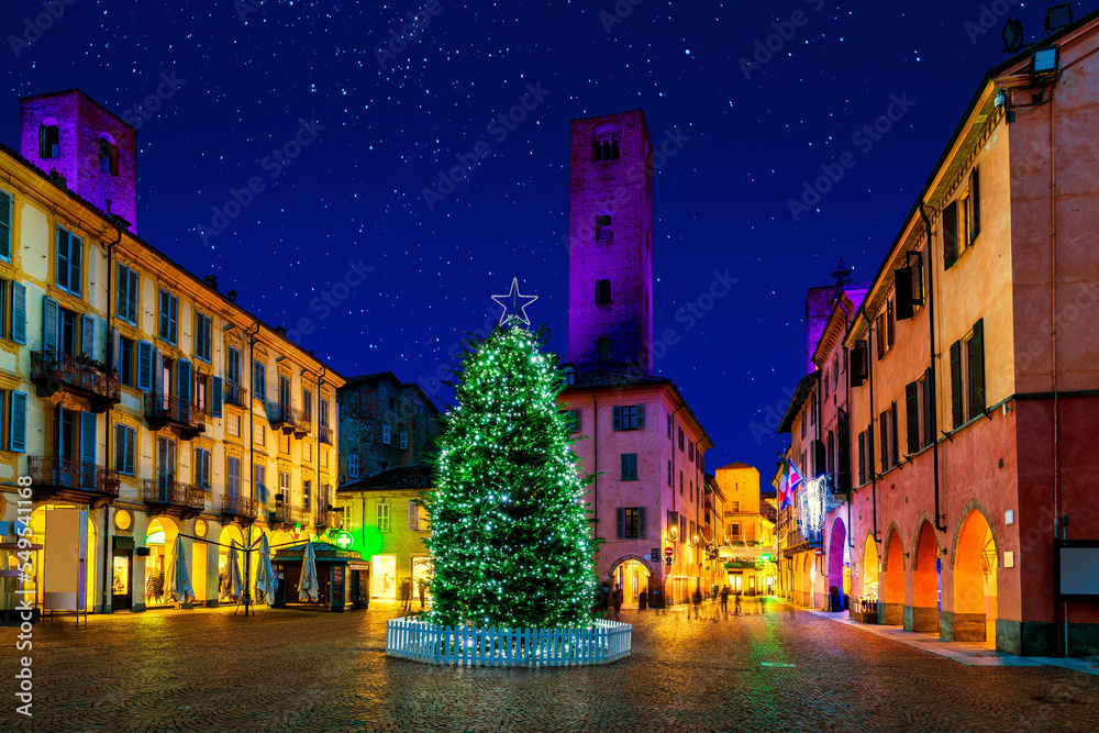 Illuminated Christmas tree on town square among old historic buildings in Alba, Italy.