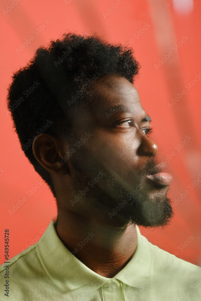 Vertical close-up cracked mirror effect studio portrait of stylish young African American man standing against salmon pink wall background looking away