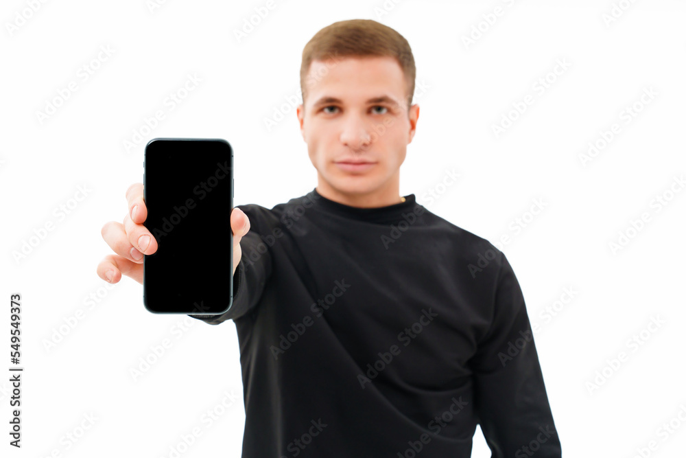 a serious man in black clothes points to a smartphone on a white background.