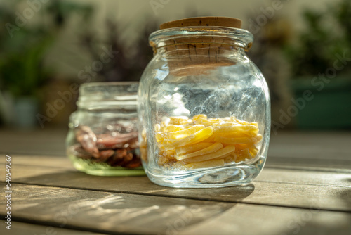 Some glass jars full of pasta with a cork stopper and another without a stopper and with dried chili peppers illuminated by a ray of morning sun