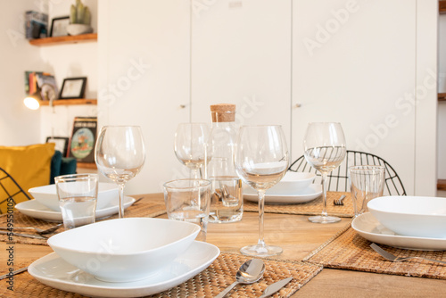 A wooden table with natural fiber placemats, crystal glasses and white porcelain dishes