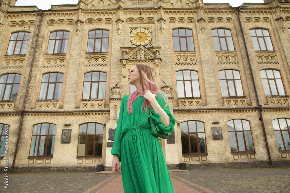 Low angle shot of an elegant woman wearing green dress, walking city streets