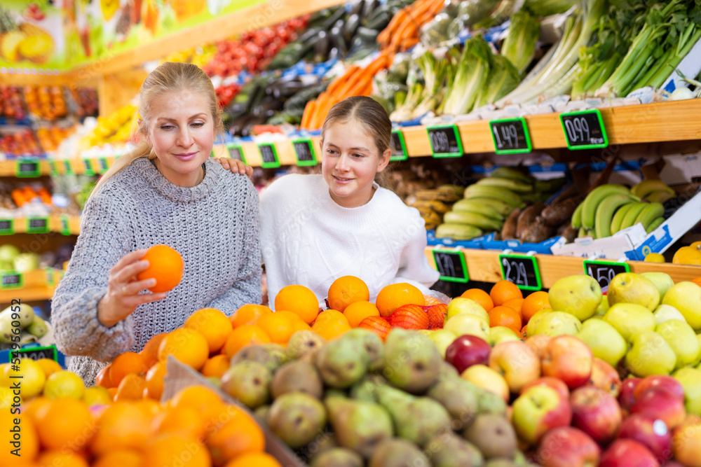 Portrait of teenage girl and her mother who buying fresh oranges at grocery shop