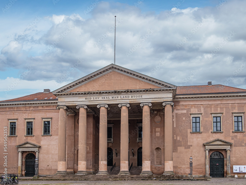 Copenhagen, Denmark - July 23, 2022: Light brown facade of Courthouse on Nytorv under blue cloudscape. Pediment and 6 tall columns. Words mean, with law, you build this land,