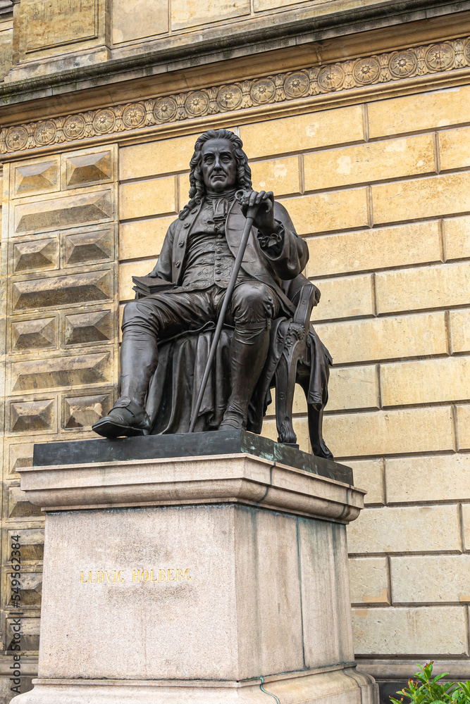 Fototapeta premium Copenhagen, Denmark - July 23, 2022: Closeup of Ludvig Holberg black statue on stone pedestal in front of Royal Theatre, yellow front facade