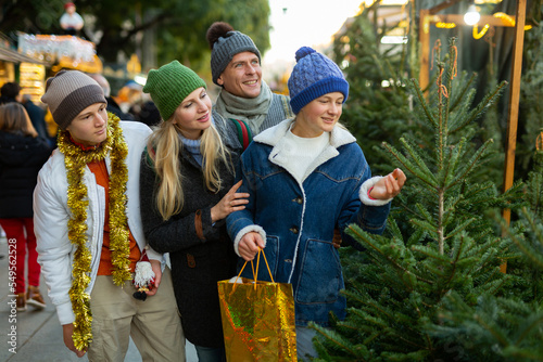 Portrait of smiling family with teenager girl and boy, choosing Christmas tree at Xmas fair