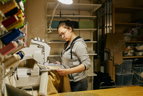 Side view shot of young woman using embroidery smart machine in tailor workshop photo