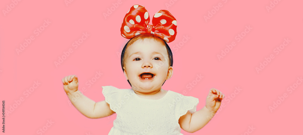 Portrait of cheerful laughing baby with bow on the head isolated on pink background