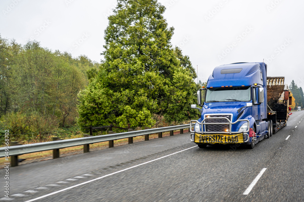 Heavy duty big rig blue semi truck tractor transporting oversized cargo