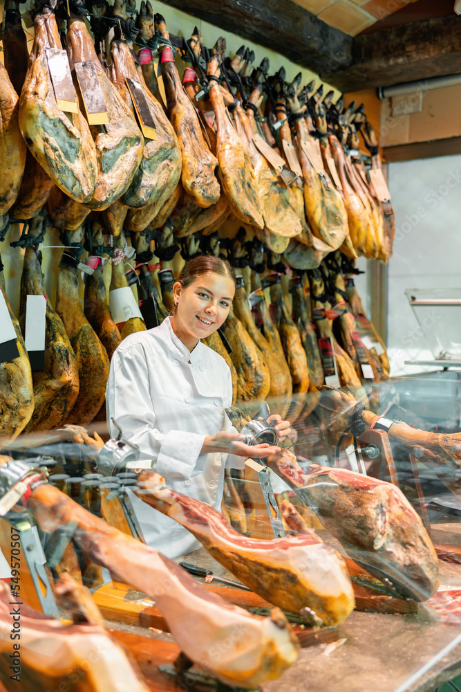 Portrait of positive young woman jamoneria worker standing at counter with arms crossed, looking at camera and smiling.