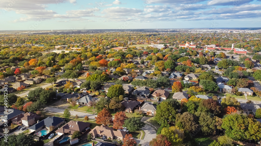 Aerial view suburban residential neighborhood under cloud blue sky with colorful fall foliage and row of single family homes near Dallas, Texas
