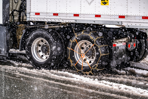 Industrial heavy big rig semi truck with semi trailer with chains on the wheels slipping slowly on a winter highway during a snowfall in the Lake Shasta region in California