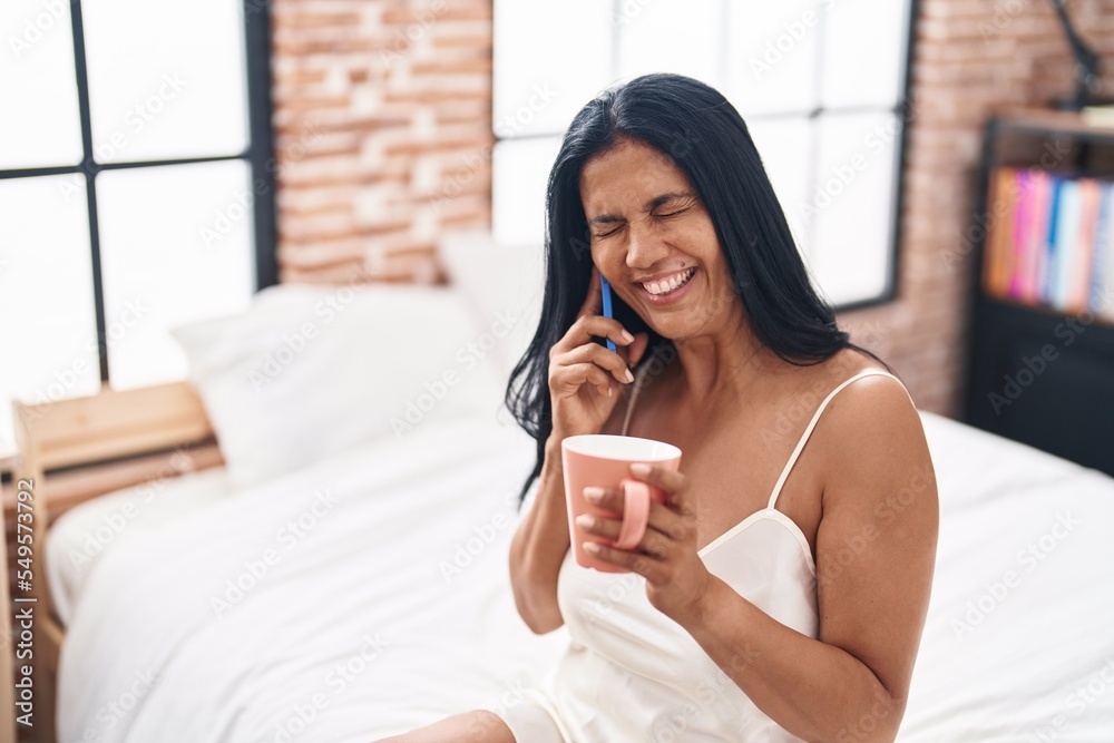 Middle age hispanic woman talking on smartphone drinking coffee at bedroom Middle age hispanic woman talking on smartphone drinking coffee at bedroom