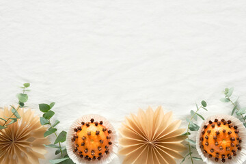 Christmas border, copy-space. Fragrant pomander balls handmade from tangerines with cloves. Handmade stars from brown baking paper. Panoramic flat lay on off white textile tablecloth with eucalyptus.