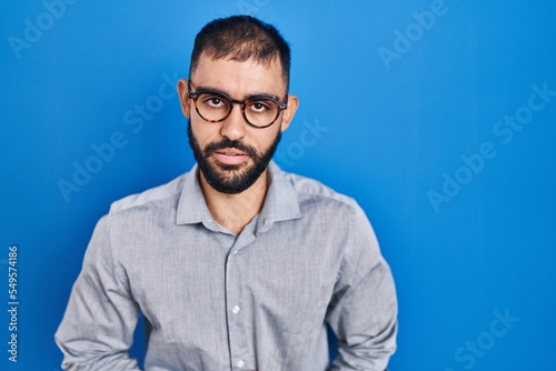 Middle east man with beard standing over blue background with hand on stomach because indigestion, painful illness feeling unwell. ache concept. © Krakenimages.com