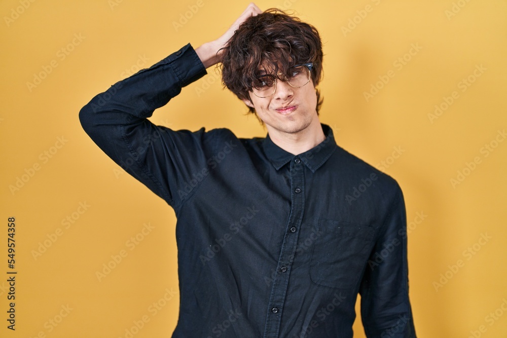 Young man wearing glasses over yellow background confuse and wonder about question. uncertain with doubt, thinking with hand on head. pensive concept. Young man wearing glasses over yellow background confuse and wonder about question. uncertain with doubt, thinking with hand on head. pensive concept.