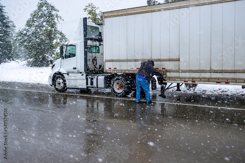 Fotografie Truck driver puts chains on the wheels of the big rig semi truck with semi trail