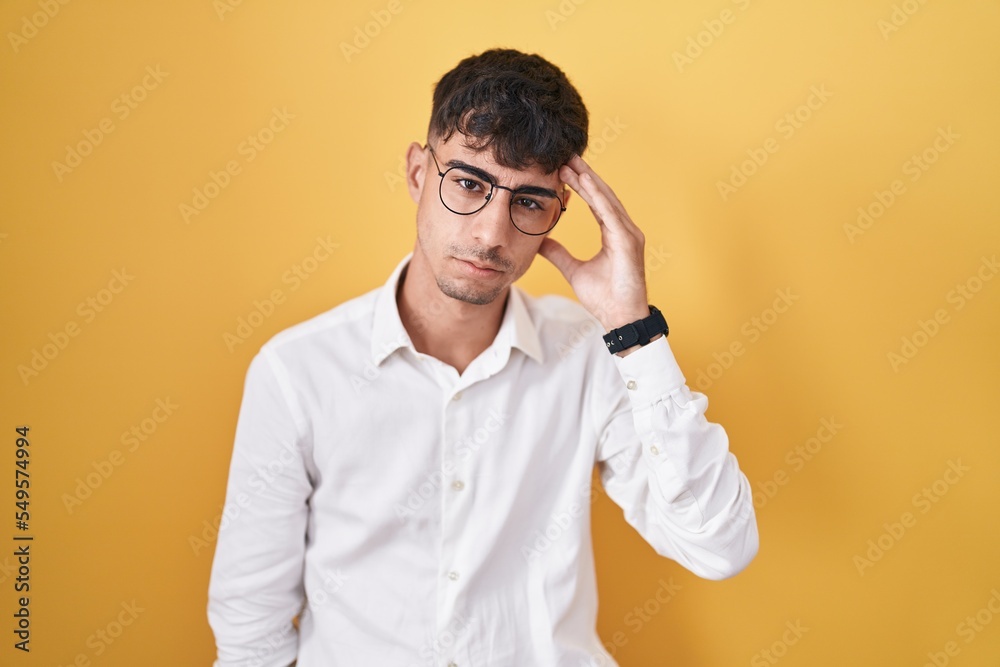 Young hispanic man standing over yellow background worried and stressed about a problem with hand on forehead, nervous and anxious for crisis Young hispanic man standing over yellow background worried and stressed about a problem with hand on forehead, nervous and anxious for crisis