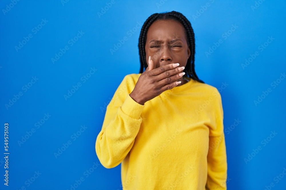 Beautiful black woman standing over blue background bored yawning tired covering mouth with hand. restless and sleepiness. Beautiful black woman standing over blue background bored yawning tired covering mouth with hand. restless and sleepiness.