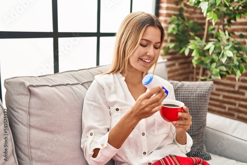 Foto Young hispanic woman drinking coffee pouring saccharin at home