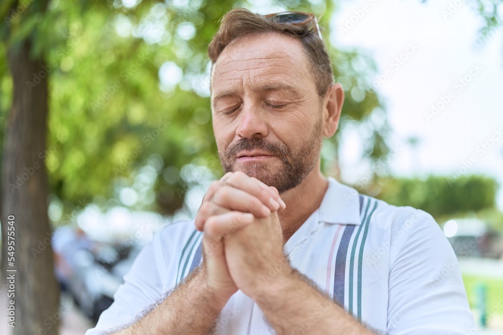 Middle age man praying with closed eyes at park Middle age man praying with closed eyes at park