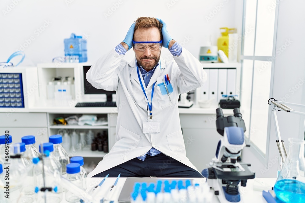Middle age man working at scientist laboratory suffering from headache desperate and stressed because pain and migraine. hands on head. Middle age man working at scientist laboratory suffering from headache desperate and stressed because pain and migraine. hands on head.