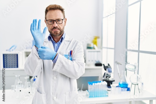 Middle age man working at scientist laboratory relaxed with serious expression on face. simple and natural looking at the camera.