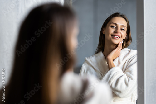 Young woman in bathrobe looking in bathroom mirror at home