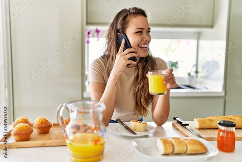 Young beautiful hispanic woman having breakfast talking on smartphone at the kitchen