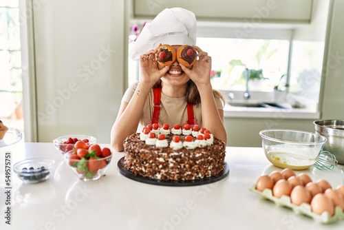 Young beautiful hispanic woman smiling confident holding cupcakes over eyes at the kitchen