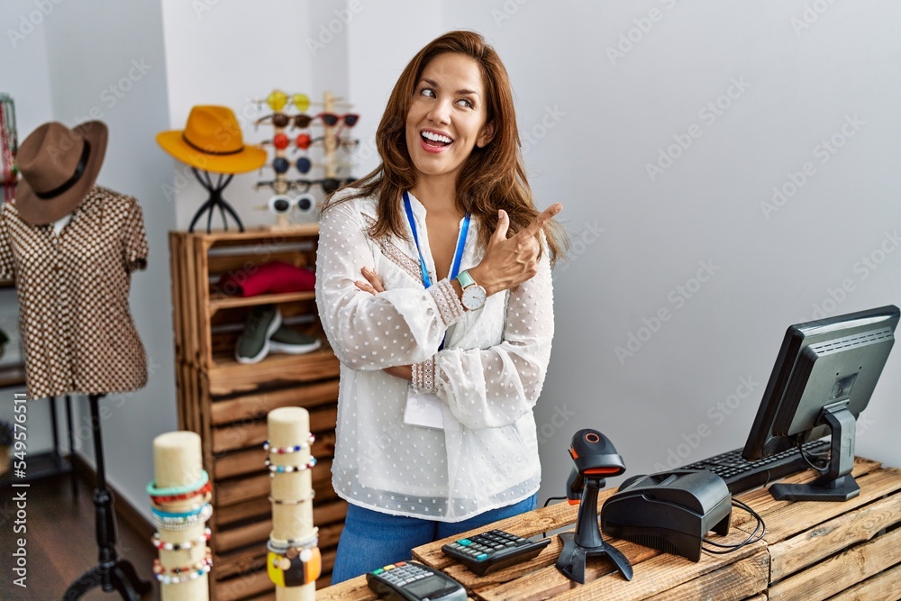Middle age hispanic woman working as manager at retail boutique with a big smile on face, pointing with hand and finger to the side looking at the camera. Middle age hispanic woman working as manager at retail boutique with a big smile on face, pointing with hand and finger to the side looking at the camera.