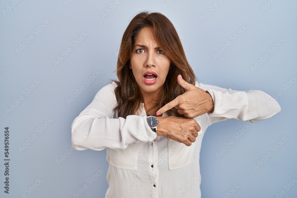 Hispanic woman standing over isolated background in hurry pointing to watch time, impatience, upset and angry for deadline delay Hispanic woman standing over isolated background in hurry pointing to watch time, impatience, upset and angry for deadline delay