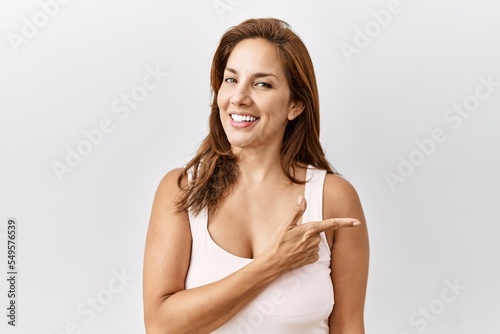 Middle age hispanic woman standing over isolated background cheerful with a smile of face pointing with hand and finger up to the side with happy and natural expression on face