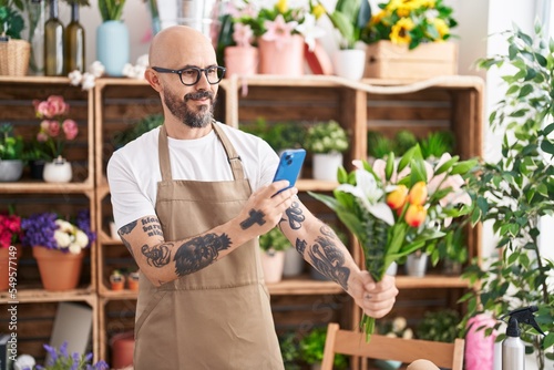 Young bald man florist make photo to flowers by smartphone at florist