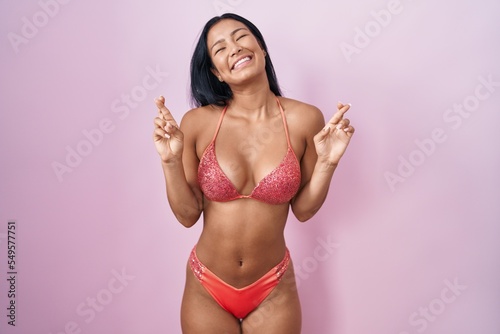 Hispanic woman wearing bikini gesturing finger crossed smiling with hope and eyes closed. luck and superstitious concept.