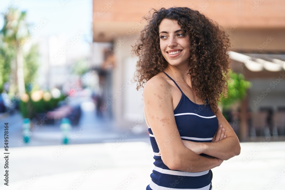 Young beautiful hispanic woman standing with arms crossed gesture at street
