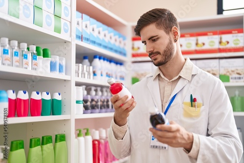 Young caucasian man pharmacist holding medication bottles at pharmacy