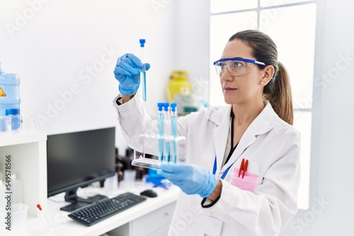 Young hispanic woman wearing scientist uniform holding test tube at laboratory