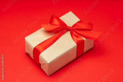 Close up shot of gift box wrapped in craft paper and decorated with satin ribbon bow, isolated on red background