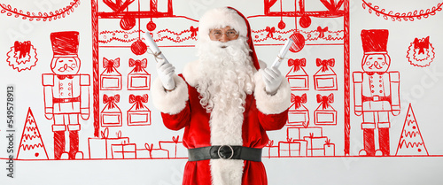 Santa Claus holding scrolls near light wall with drawings