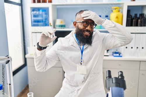 African american man working at scientist laboratory holding syringe stressed and frustrated with hand on head  surprised and angry face