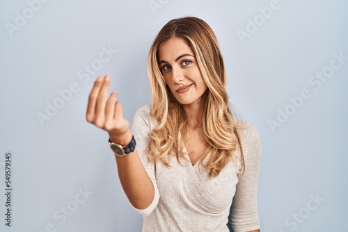 Young blonde woman standing over isolated background doing italian gesture with hand and fingers confident expression