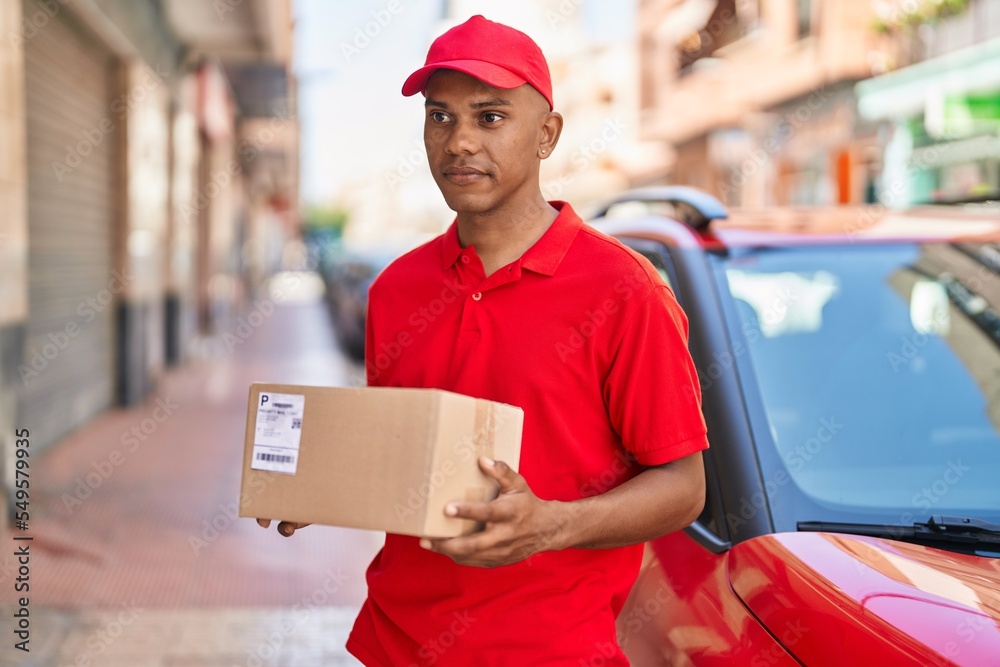Young latin man delivery worker holding package at street Young latin man delivery worker holding package at street