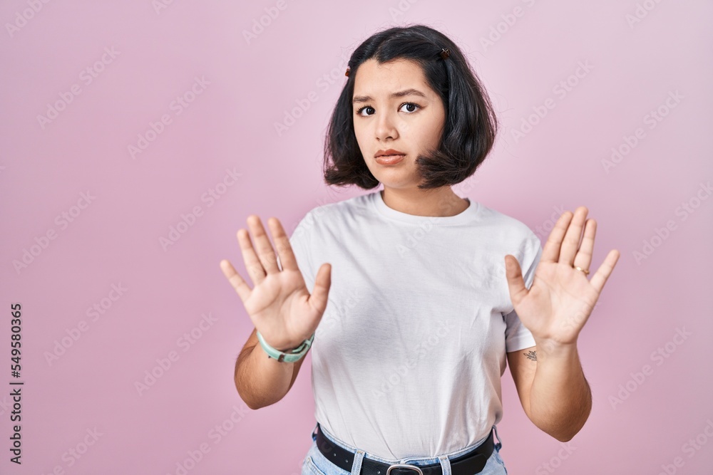 Young hispanic woman wearing casual white t shirt over pink background moving away hands palms showing refusal and denial with afraid and disgusting expression. stop and forbidden. Young hispanic woman wearing casual white t shirt over pink background moving away hands palms showing refusal and denial with afraid and disgusting expression. stop and forbidden.