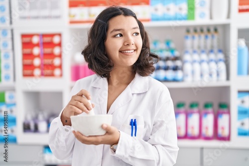 Young woman pharmacist smiling confident mixing medicine at pharmacy