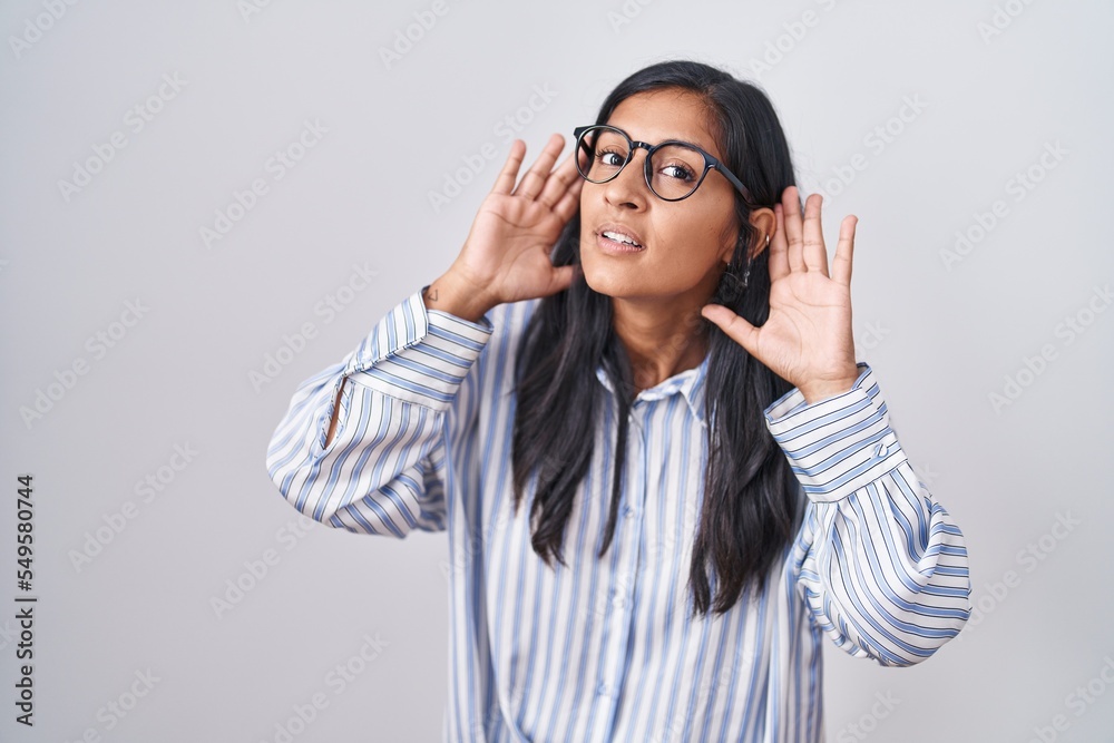 Young hispanic woman wearing glasses trying to hear both hands on ear gesture, curious for gossip. hearing problem, deaf Young hispanic woman wearing glasses trying to hear both hands on ear gesture, curious for gossip. hearing problem, deaf
